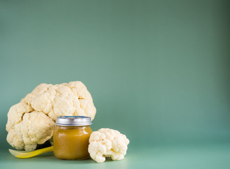 Glass jar with natural baby food on the table: vegetable puree with cauliflower selective focusの写真素材