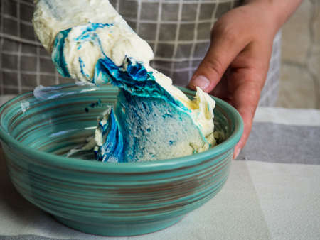 a girl makes a colored cream for a cake using liquid food coloringの写真素材