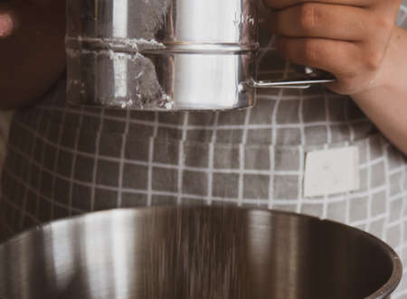 The girl's hand holds a metal sifter of flour, flour is sprinkled through a sieve. Sifting flour....