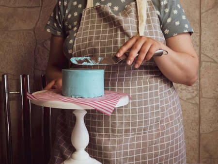 pastry chef girl spreads cream with a spatula on a freshly baked birthday cakeの写真素材
