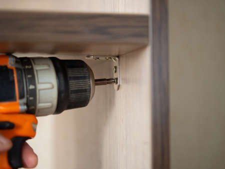 assembles furniture with a black and orange cordless screwdriver. Power tools for construction and...