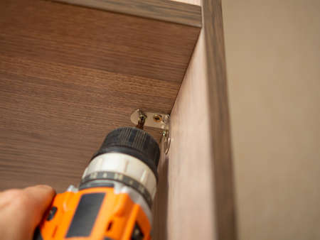 assembles furniture with a black and orange cordless screwdriver. Power tools for construction and...