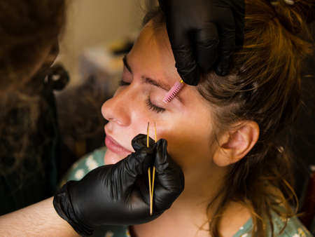 Permanent makeup. Beautiful young woman receiving eyebrow correction procedure. Tweezing a girl's...