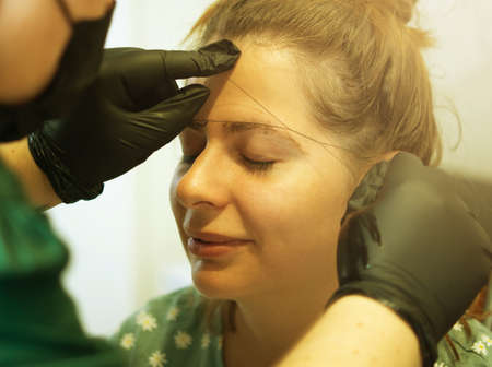 Make-up artist plucking eyebrows with a thread Professional face care.