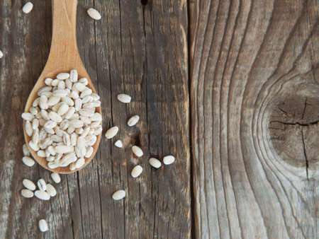 raw pearl barley in a wooden spoon spilling on an old wooden tableの写真素材