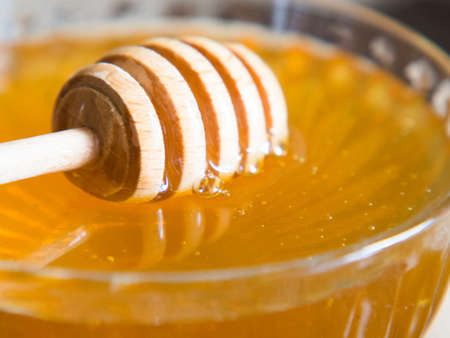 Honey drips from a honey dipper into a beautiful glass bowl. Close-up. Healthy organic thick honey and combs.の写真素材