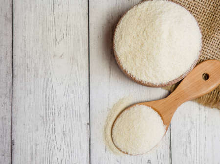 Semolina in a wooden bowl and spoon on a white wooden table, close-up. healthy diet cereals background.の写真素材