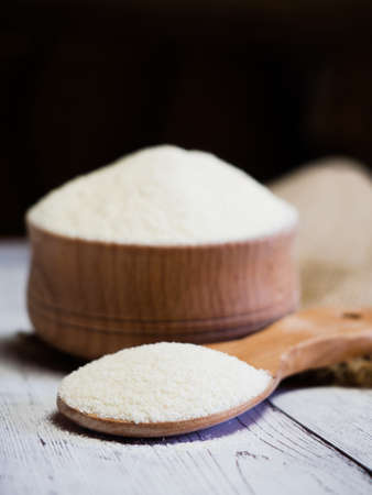 Semolina in a wooden bowl and spoon on a white wooden table, close-up. healthy diet cereals background.の写真素材