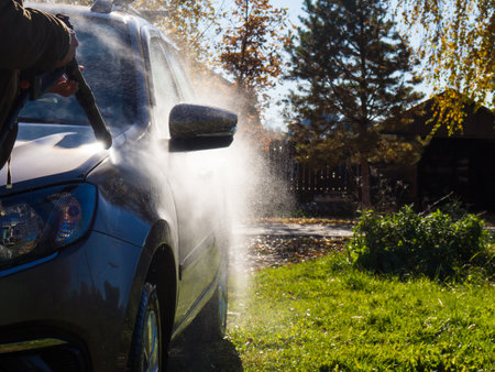 the girl washes the car at home near the garage using a pressure washerの写真素材