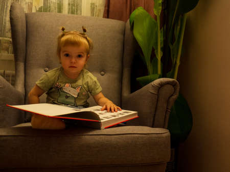 little girl leafing through a book while sitting in a chair life style