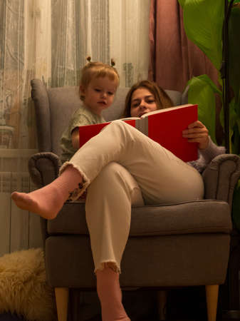 mom and daughter read a book in a chair lifestyleの写真素材