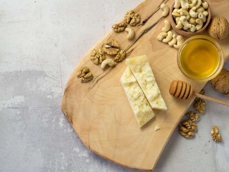 slices of hard cheese on a wooden board with nuts and honey the best combinationの写真素材