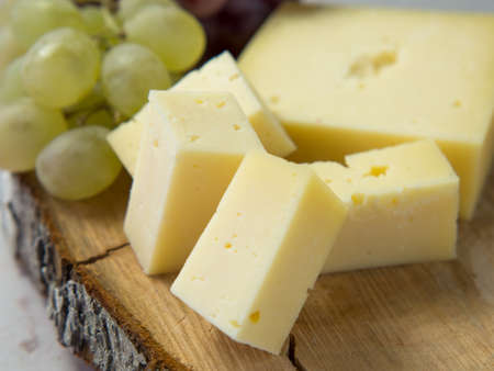 Light meal with sliced cheese next to a bunch of white and red grapes
