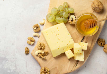 farm-quality cheese lies on a wooden board surrounded by grapes. nuts and honey close-up on a light backgroundの写真素材