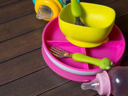bright multi-colored children's tableware. spoon fork bowls and sippy cups on wooden tableの写真素材