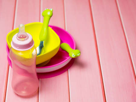 bright multi-colored children's tableware. spoon fork bowls and sippy cups on wooden tableの写真素材