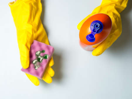 woman in yellow gloves pours dishwashing gel onto a sponge. housework in the kitchen.