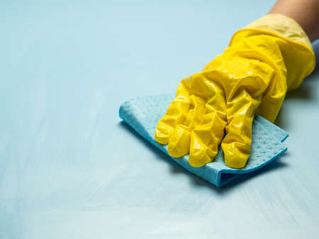 A hand in a yellow rubber glove holds a cleaning sponge in soapy foam on a blue background. House cleaning concept, cleaning serviceの写真素材
