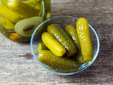 Pickled cucumbers in a bowl on a wooden rustic table and a jar of picklesの写真素材
