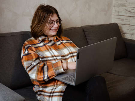 young girl in glasses working on a laptop sitting at home on the bed.