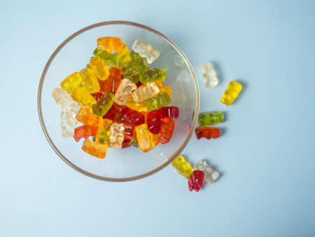 Bowl with tasty bright gummy bears on blue tableの写真素材