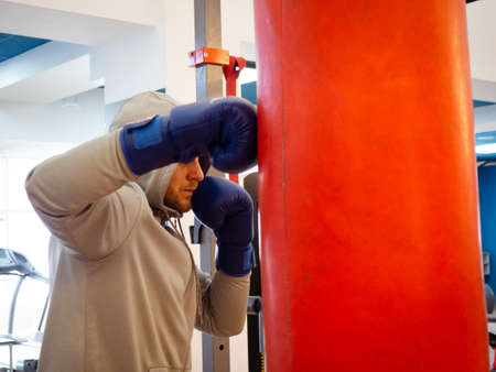 Boxing training - a hand and a red punching bag. a guy in a hood hits a punching bag