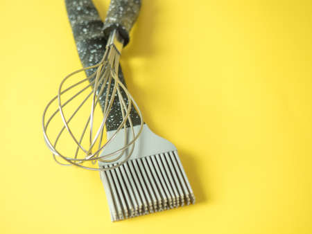 whisk and oil brush on yellow background.cooking concept