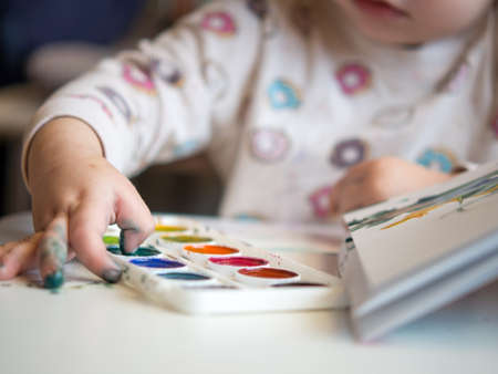 The girl sits at the table and draws with her fingers in the sketchbook. children's creativity. Children's hobbies.の写真素材