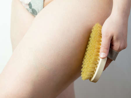 close-up Woman doing leg massage with wooden soft massage brush for body and legs. Cellulite prevention, skin care.の写真素材