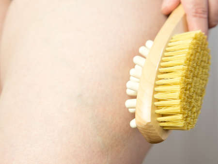 close-up Woman doing leg massage with wooden soft massage brush for body and legs. Cellulite prevention, skin care.の写真素材