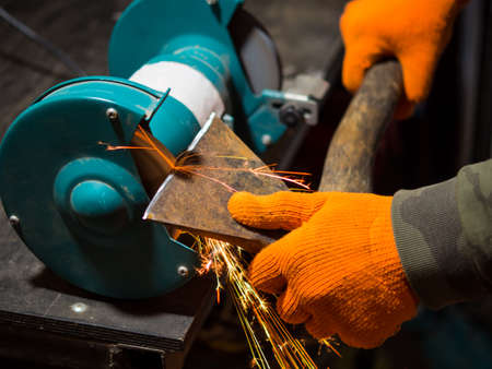 man sharpening an ax blade on a grinderの写真素材