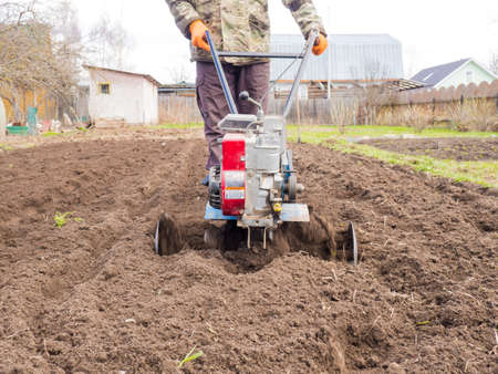 A man works the land in the garden with a cultivator, prepares the soil for sowing. farming conceptの写真素材