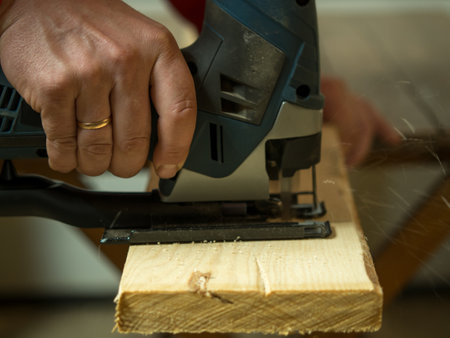 a man saws a board with an electric jigsaw close-up .hand electric saw ,the concept of working with woodの写真素材