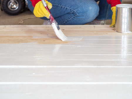 brush with white paint in the hand of a girl close-up, the girl paints a wooden surfaceの写真素材