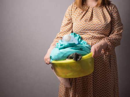 Portrait of a girl in glasses with a basin of dirty laundry and washing powder, a housewife girl...