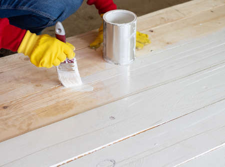 brush with white paint in the hand of a girl close-up, the girl paints a wooden surfaceの写真素材