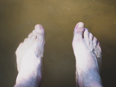 men's legs are lowered in muddy river water close-upの写真素材