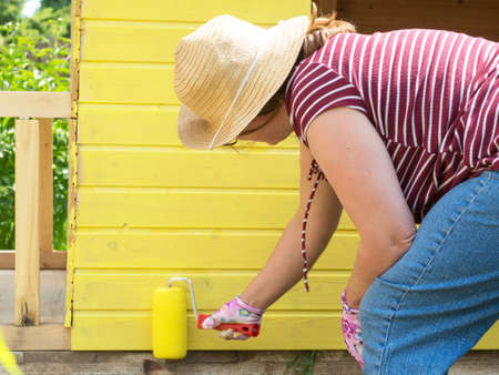 young girl paints a wooden wall with a roller with yellow paintの写真素材
