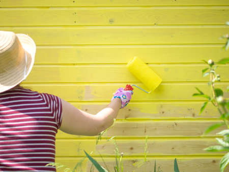 young girl paints a wooden wall with a roller with yellow paintの写真素材