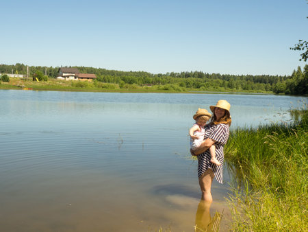 A young mother holds her little daughter in her arms while swimming in the lake. Summer activities in the family. mother teaches child to waterの写真素材