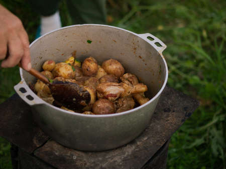 dinner on the fire, potatoes with zucchini and chicken are cooked in a cauldron on the streetの写真素材