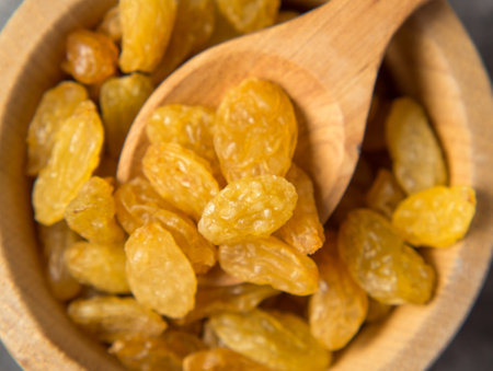 Golden raisins in a wooden bowl and a spoon on a dark concrete background. Dried grapes or raisins.の写真素材