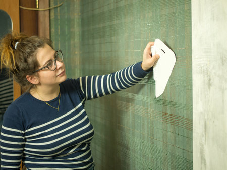 girl gluing wallpaper at home, smoothing out new wallpaper with a plastic spatulaの写真素材