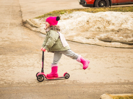 child rides a pink scooter on a spring day
