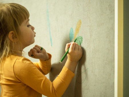 cute little girl draws with a colored pencil on the wall. Children's work,little girl draws with a felt-tip pen on the wallpaper at homeの写真素材