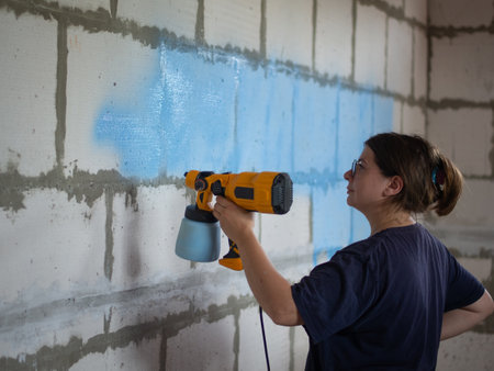 girl paints concrete wall blue with spray gunの写真素材