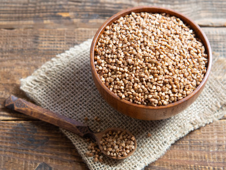 Organic buckwheat groats in a wooden bowl with a spoon on a linen napkin on a wooden table.の写真素材