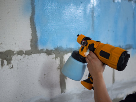 girl paints concrete wall blue with spray gunの写真素材