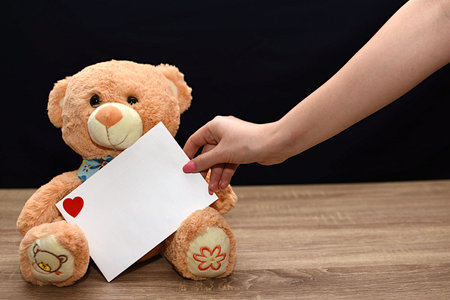 A teddy bear is on the table and the girl holds out a white envelope with a heart. Valentine's Day giftの写真素材