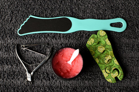 set for pedicure and manicure at home. tweezers, nail file, pink scrub and a divider for the hoop against the background of a gray towel. SPA at home, with your own hands.の写真素材